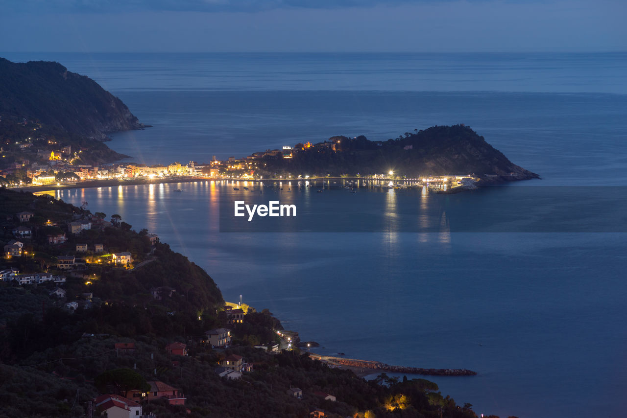 Illuminated city by sea against sky at night, liguria, italy