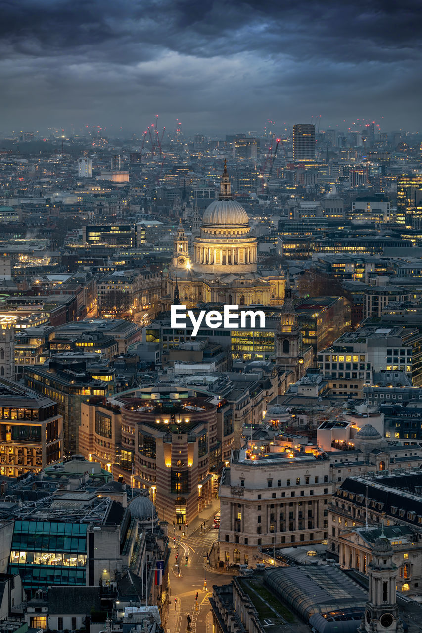 Aerial view of illuminated buildings against cloudy sky in city at dusk