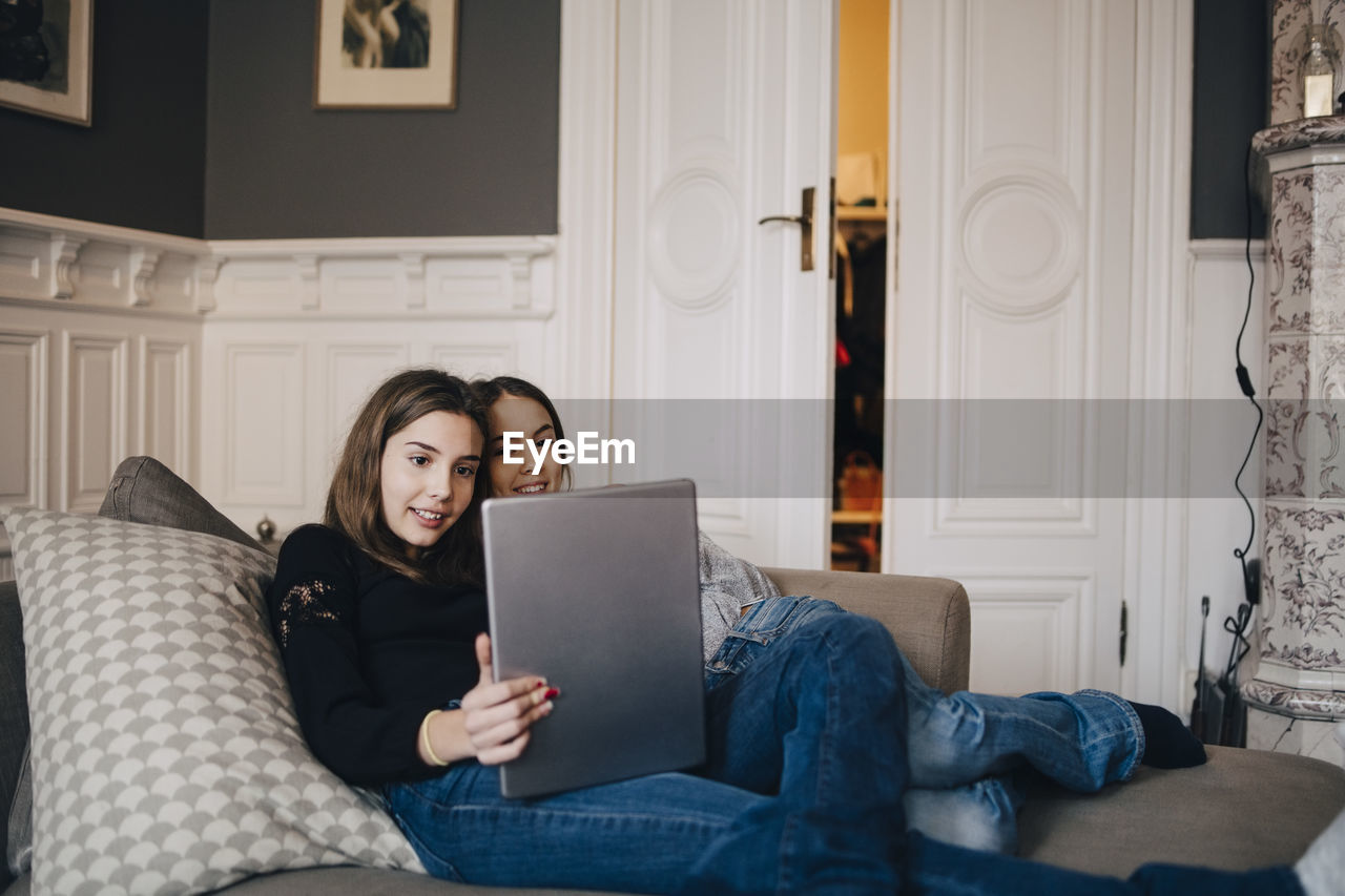 Smiling girls using laptop while resting on sofa at home