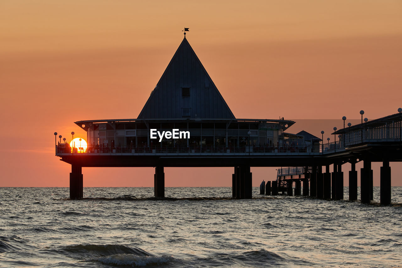 sunset, architecture, water, sky, built structure, evening, sea, dusk, nature, ocean, horizon, building exterior, travel destinations, beauty in nature, pier, transportation, travel, reflection, building, twilight, beach, no people, coast, sun, silhouette, scenics - nature, outdoors, city, motion, tower, orange color, land, tranquility, idyllic, bridge, tourism, horizon over water