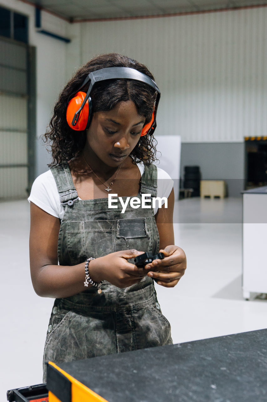 Professional young african american female mechanic in apron and protective headphones taking tools from box while working in modern repair service workshop