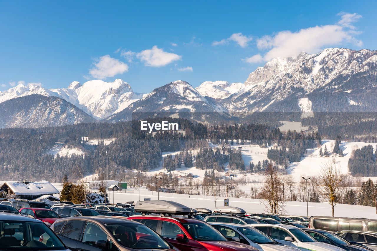 Car parking and aerial view of snowcapped mountains against sky. 
