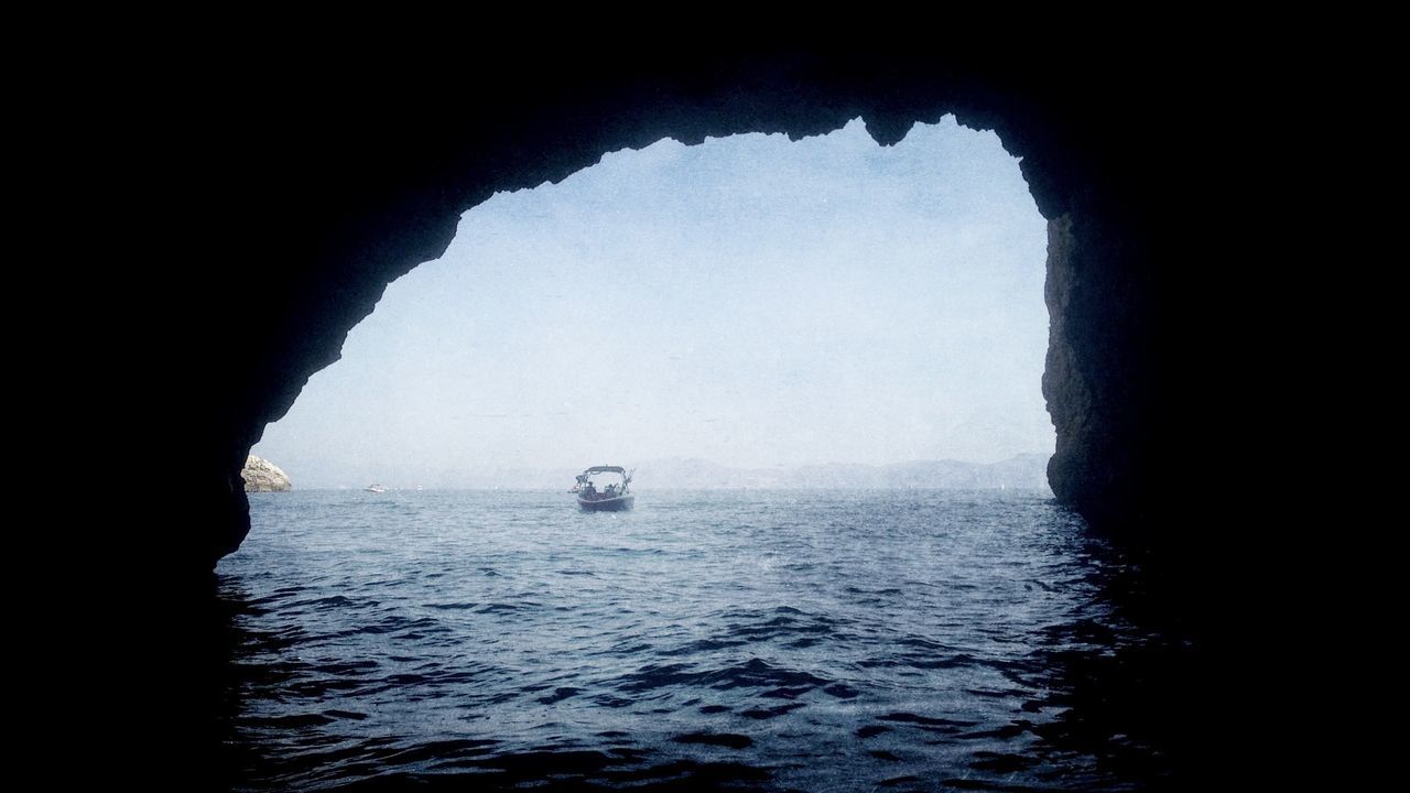 Boat sailing in sea seen from natural arch