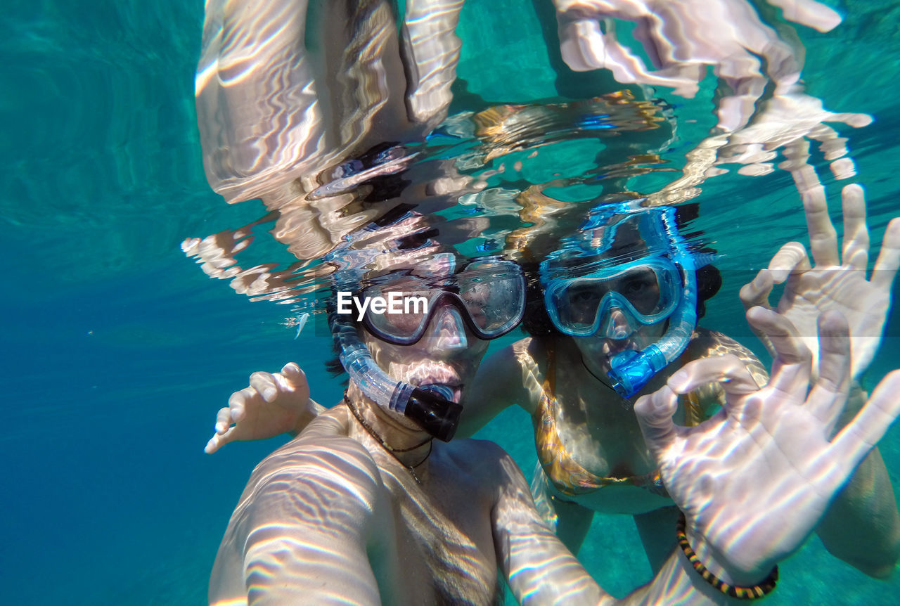 Couple showing ok sign while snorkeling in sea