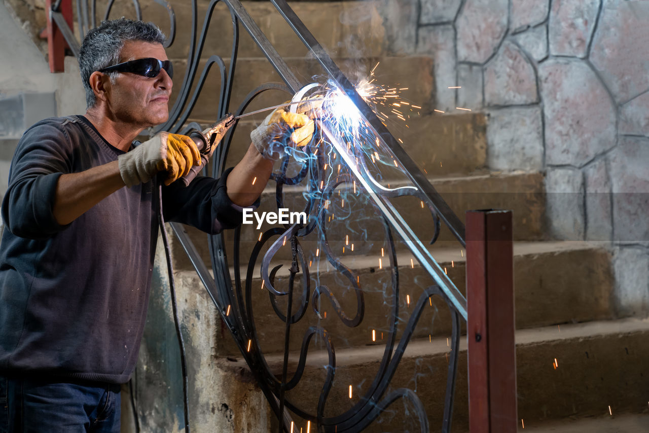 Man wearing protective glasses welds metal with welding machine. sparks from welding fly to sides.