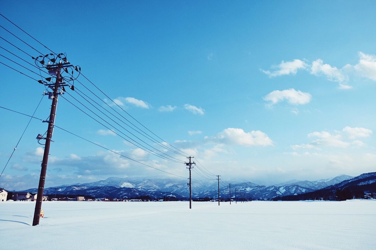 Snow covered electricity pylon against sky
