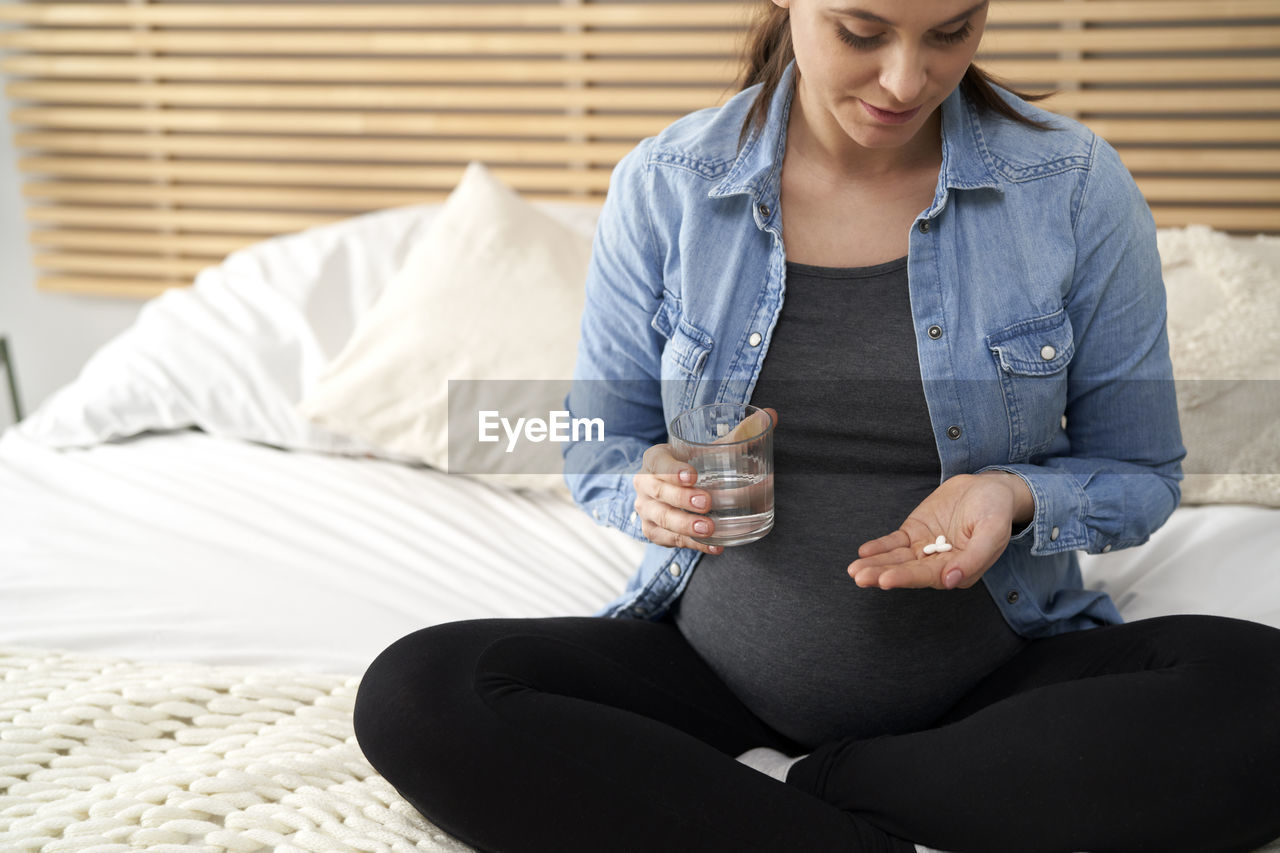 Midsection of pregnant woman taking tablet at home