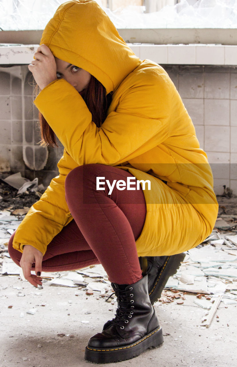 Young woman in yellow hood jacket knelt down