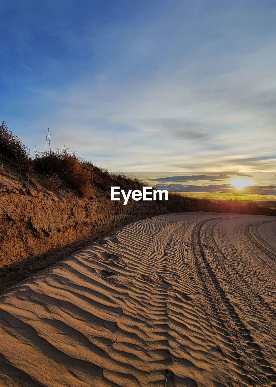 sky, landscape, land, natural environment, sand, scenics - nature, horizon, nature, environment, beauty in nature, sunset, cloud, sunlight, tranquility, field, desert, no people, sand dune, tranquil scene, non-urban scene, soil, sun, outdoors, plant, travel, arid climate, horizon over land, travel destinations, day, tire track, remote, blue, rural scene, dry, climate, plain