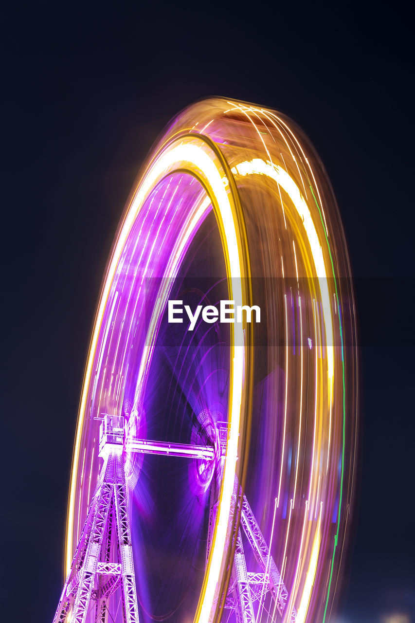 Low angle view of illuminated ferris wheel spinning against sky at night