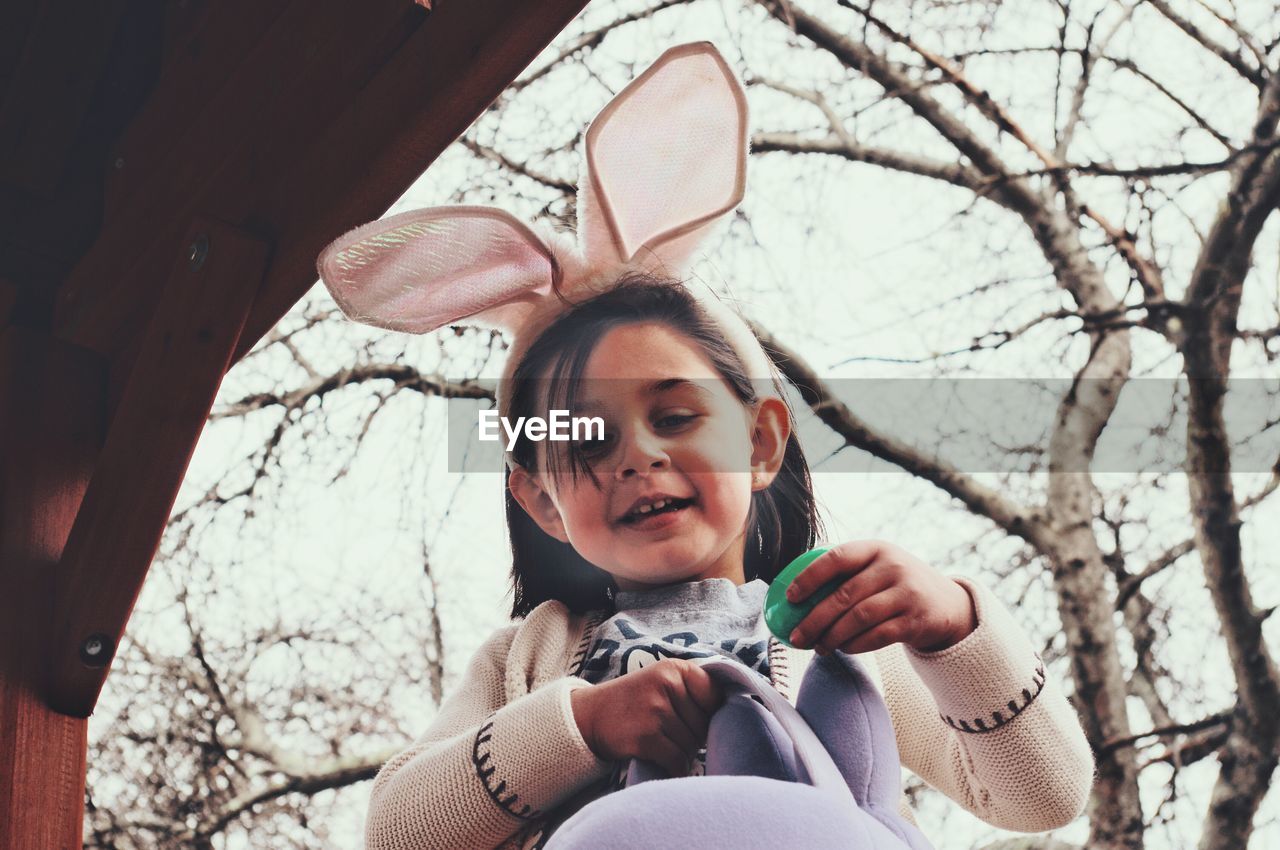 Low angle view of girl holding easter egg by bare tree