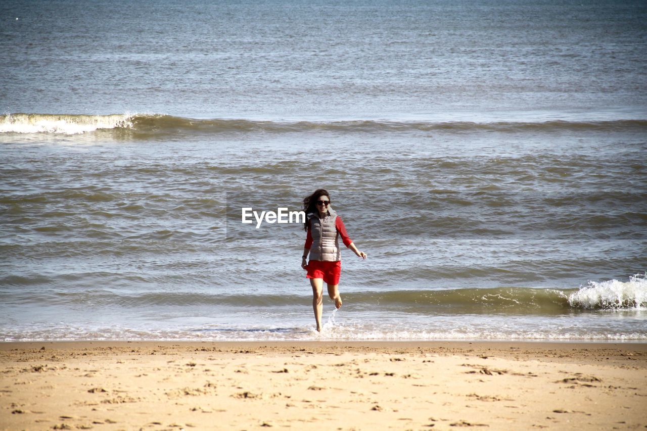 Young woman running at beach against clear sky