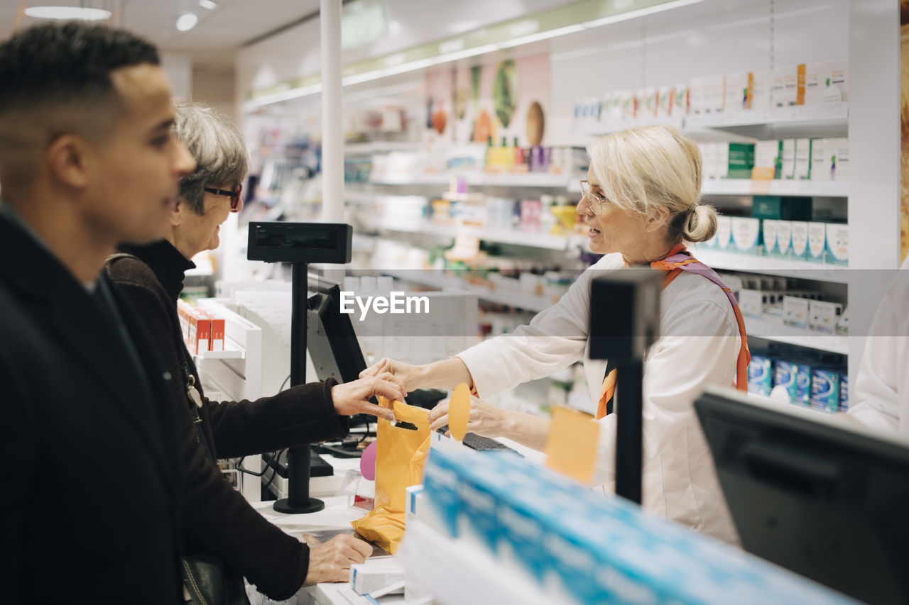 Pharmacists and customers standing at checkout in medical store