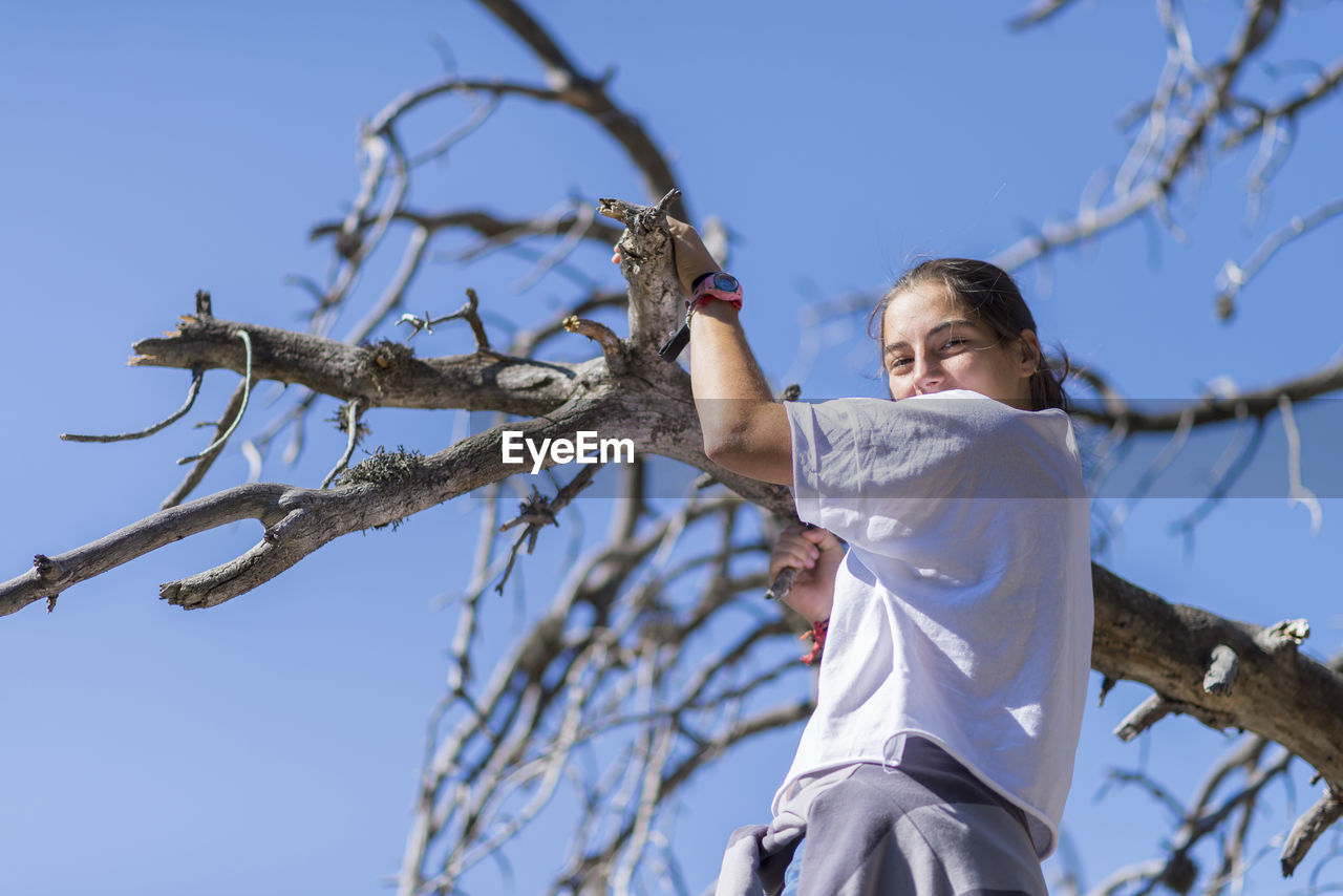 Low angle view of woman holding branch against blue sky