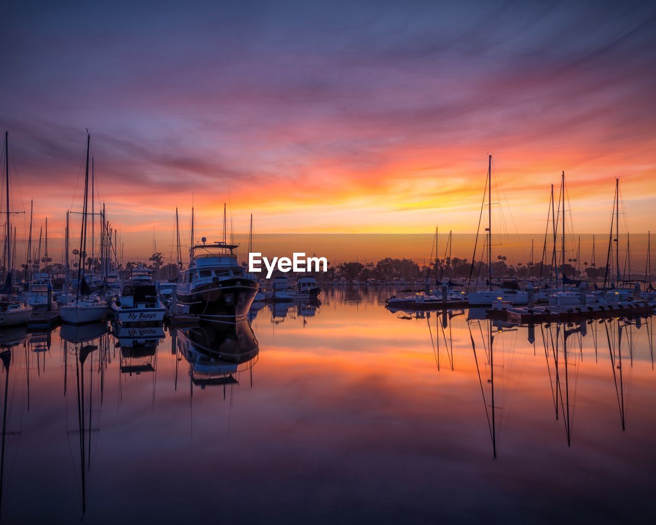 Sailboats moored at harbor during sunset