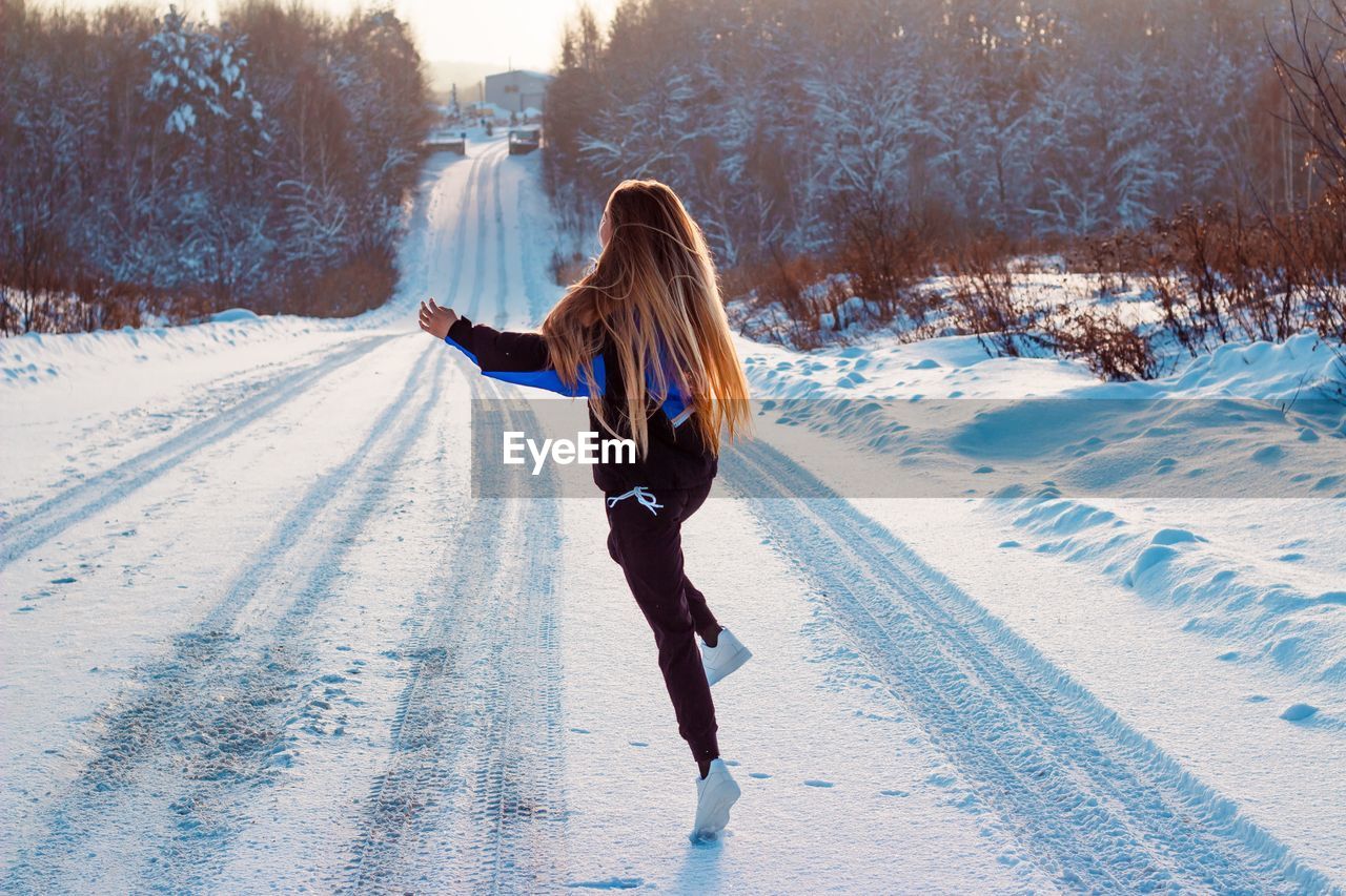 Rear view of woman jumping on snow covered field