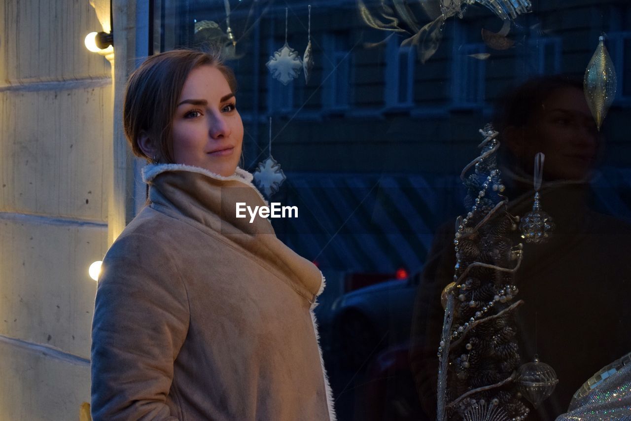 Thoughtful woman wearing warm clothing while standing by display cabinet during christmas at night