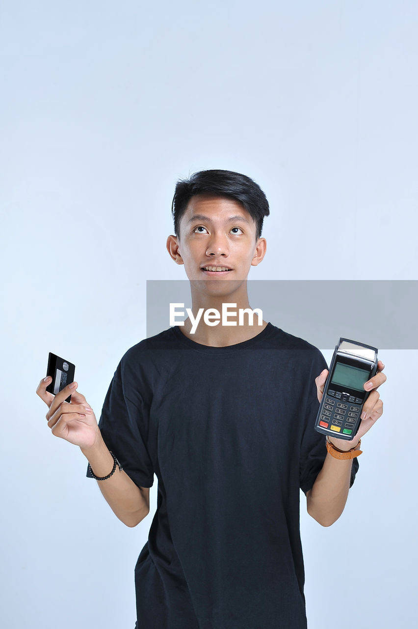 Young asian man showing a credit card / a debit card and an electronic data capture (edc) machine for easy and fast financial transaction