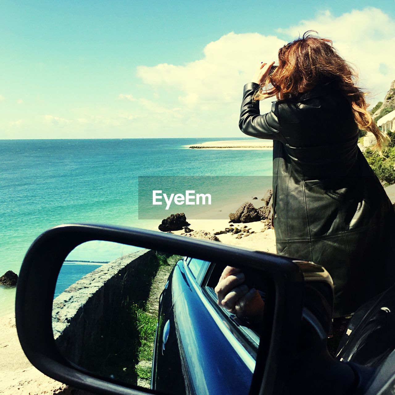 Rear view of woman on car photographing sea
