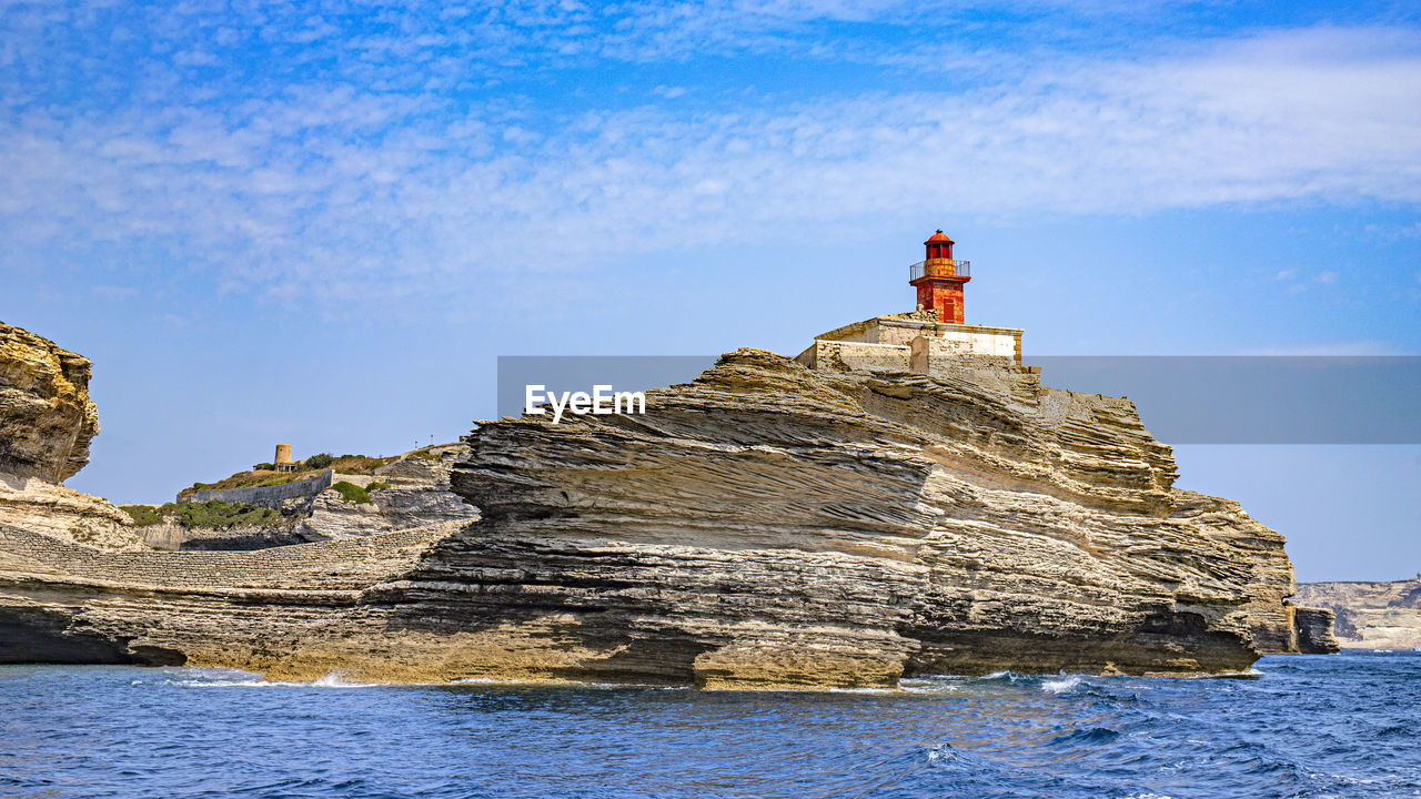 LIGHTHOUSE ON ROCK BY SEA AGAINST BLUE SKY