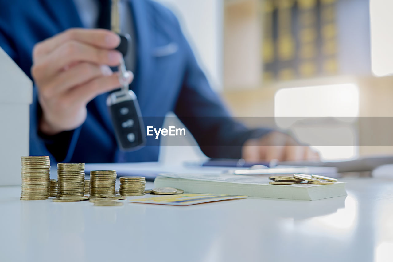 Midsection of man holding car key by coins on table