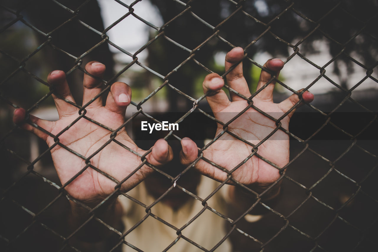 Cropped image of man touching metal fence