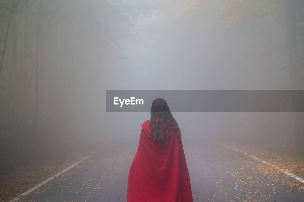 Rear view of woman standing on road in foggy weather