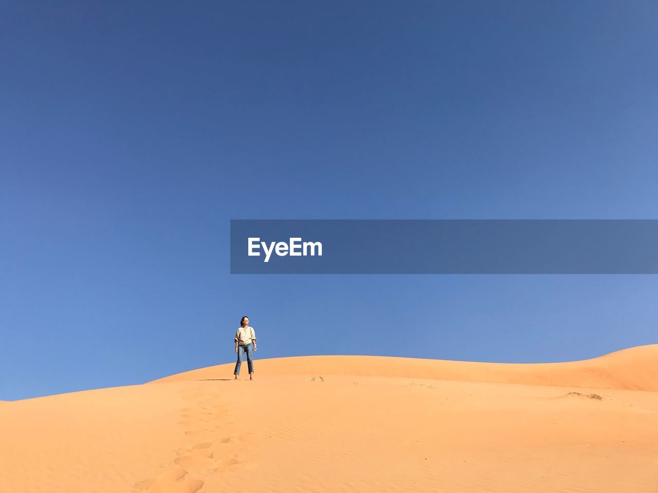 Woman standing at desert against clear blue sky