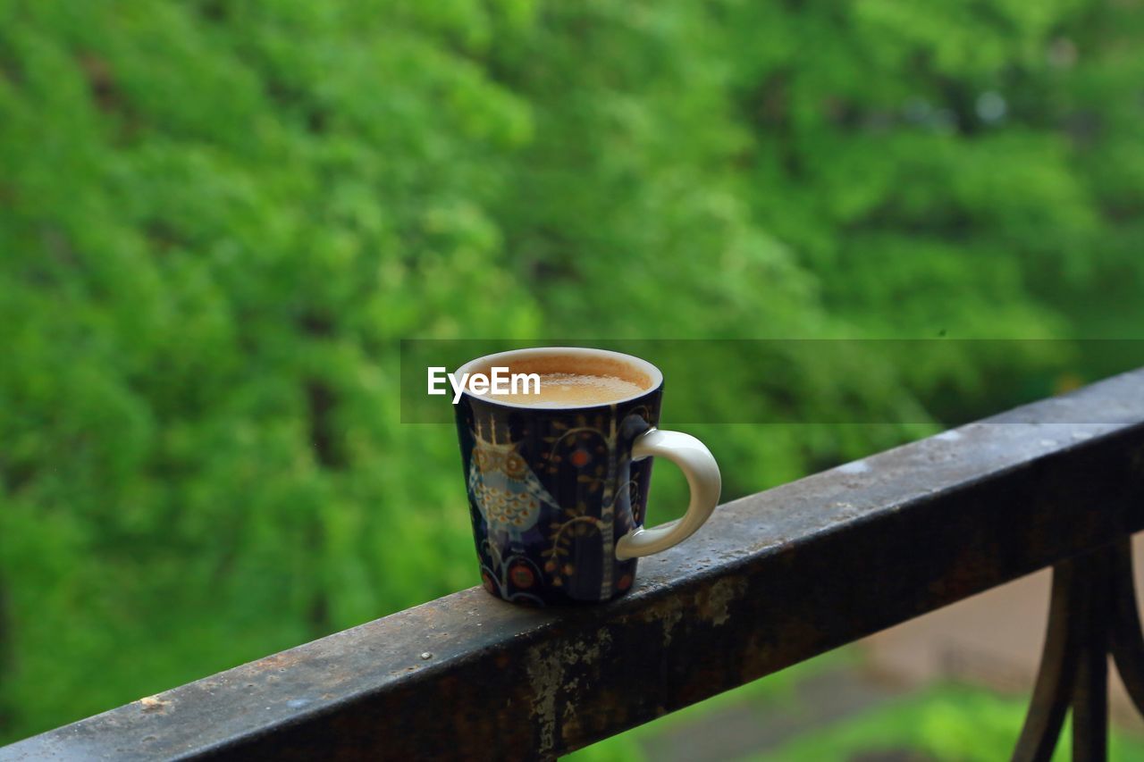 Close-up cup of coffee on railing against blurred background