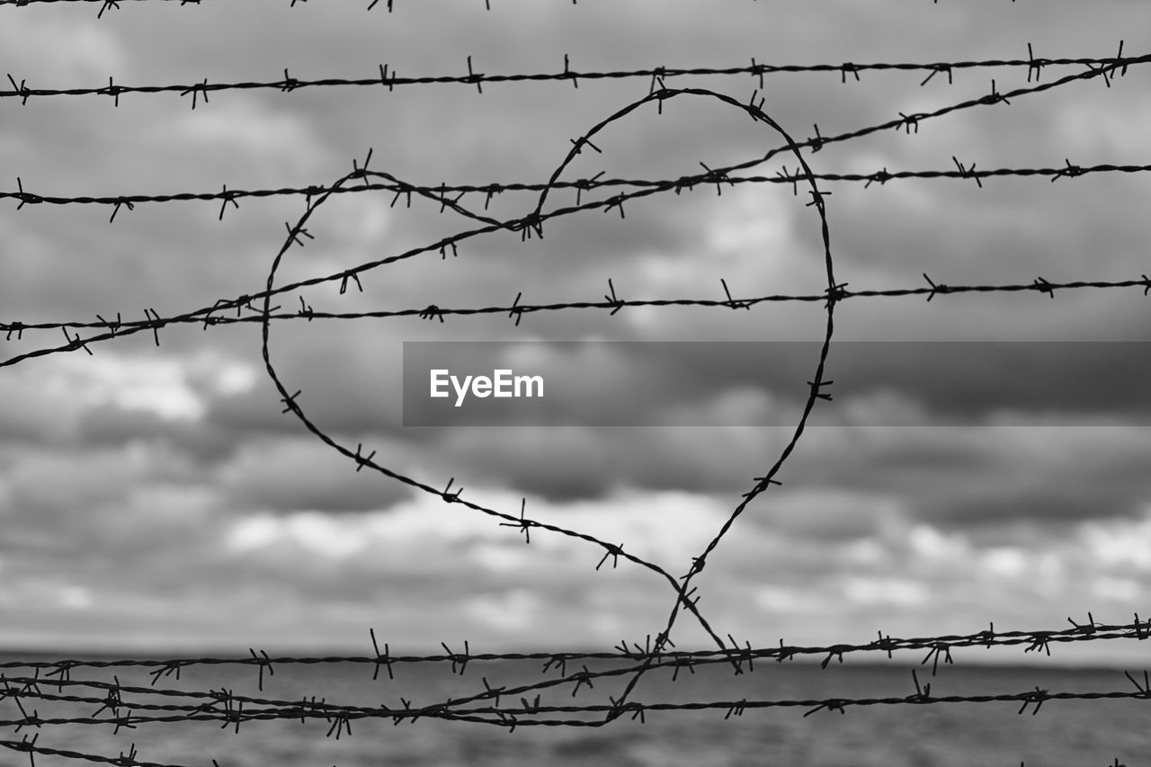 Low angle view of barbed wire fence against sky