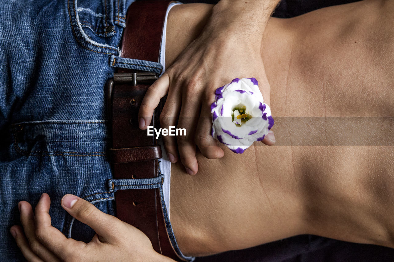 Midsection of shirtless man holding flower while lying on bed at home