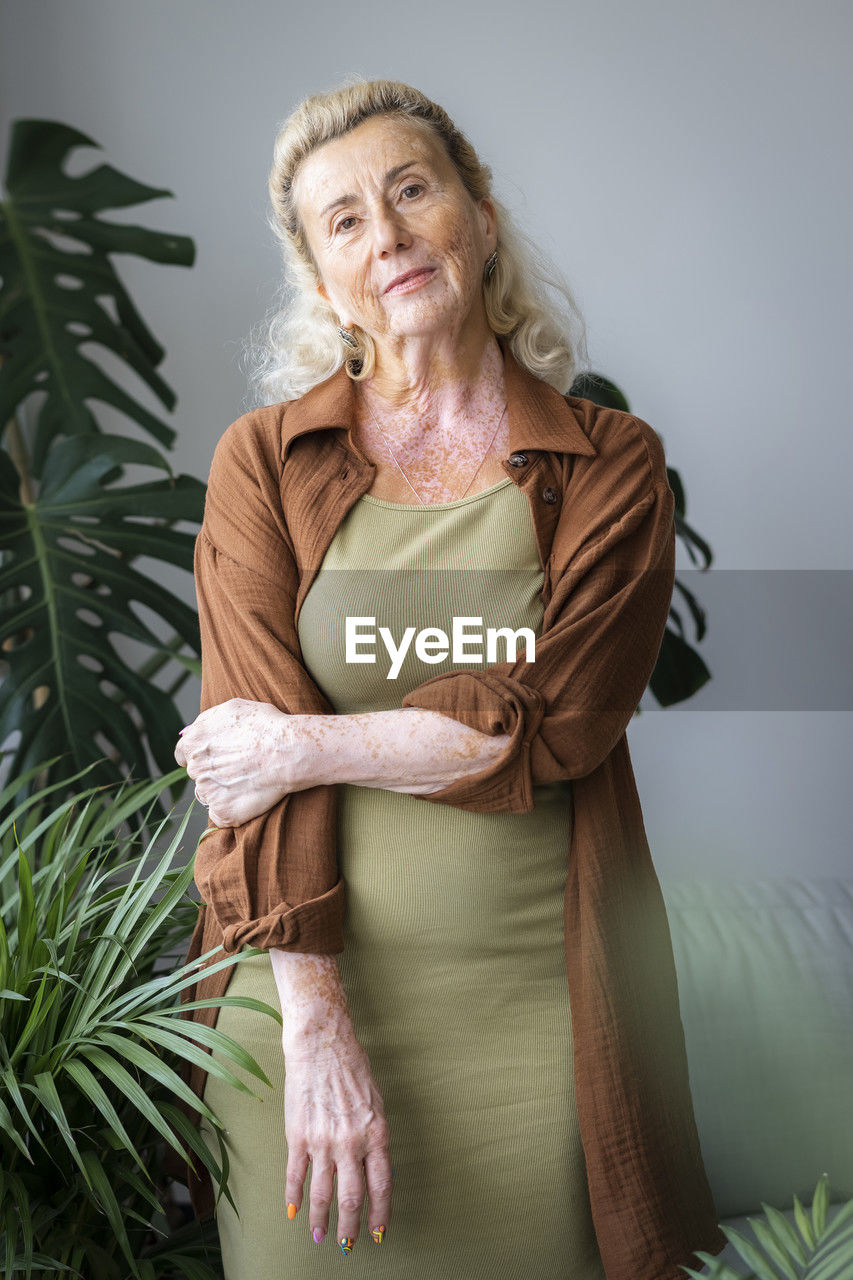 Confident senior woman standing near plants at home