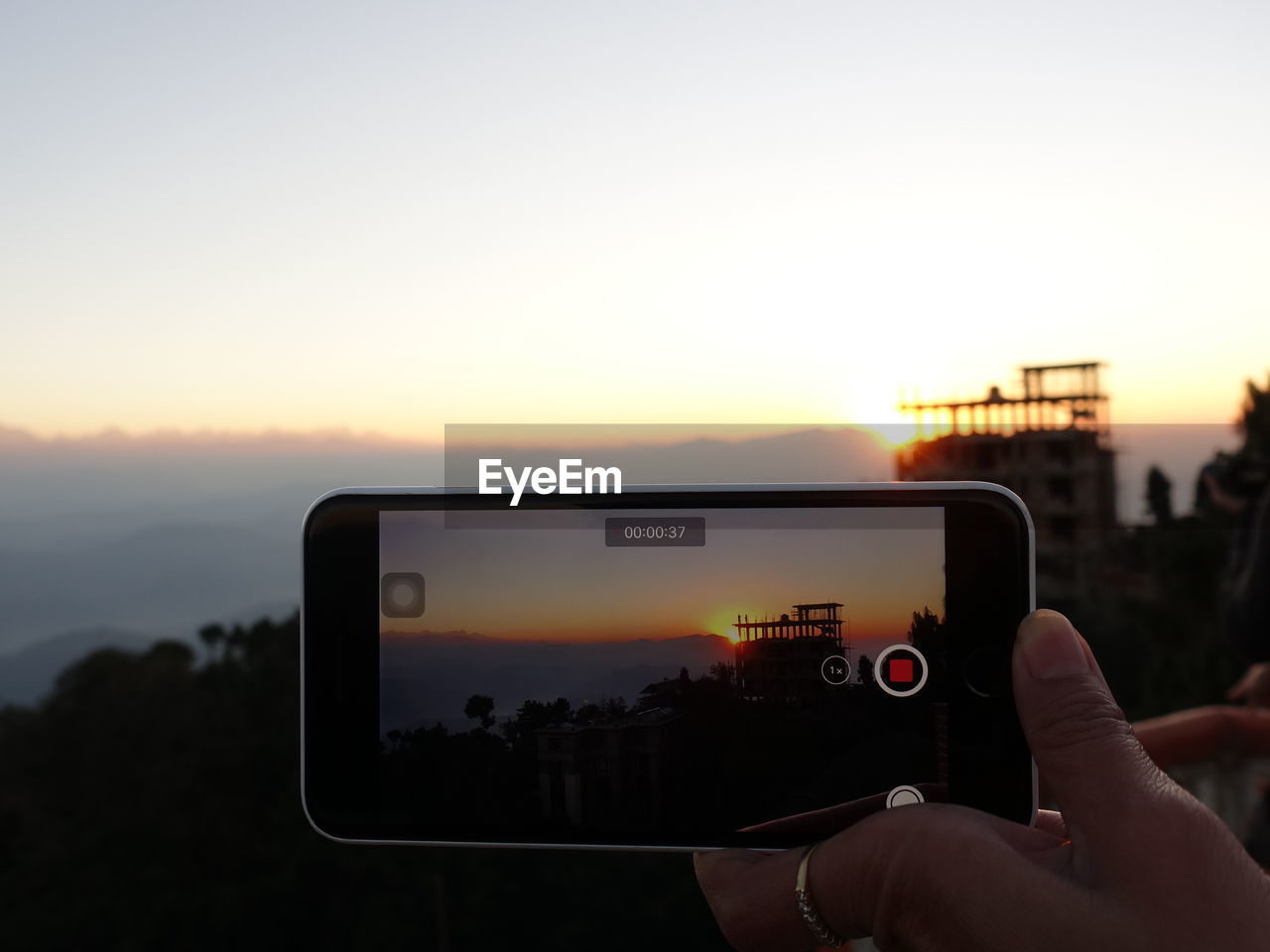 MAN PHOTOGRAPHING USING SMART PHONE AGAINST SKY