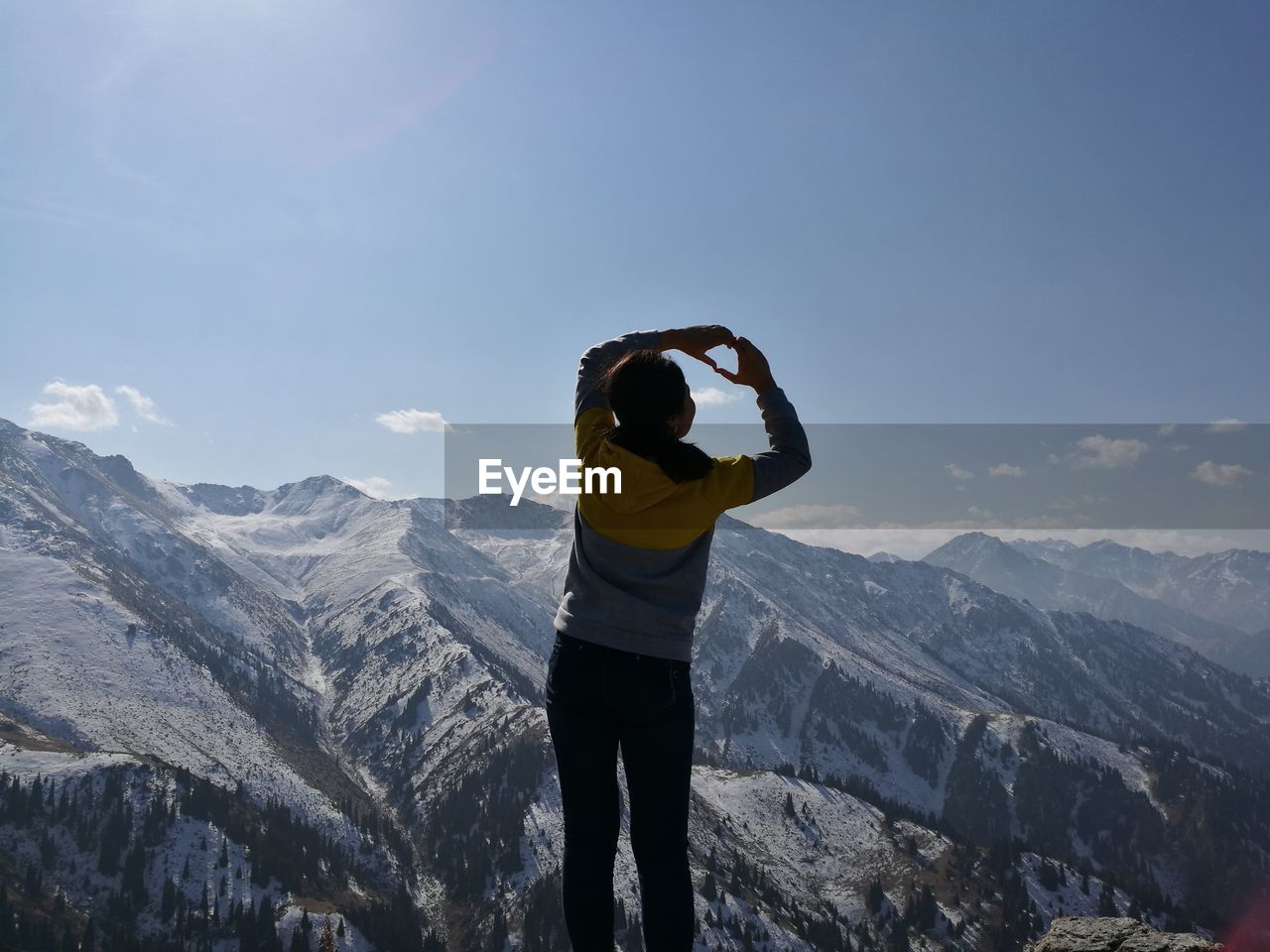 Rear view of woman making heart shape while standing on mountain