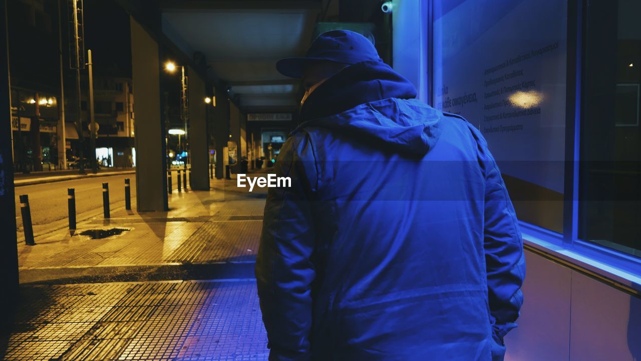 Rear view of man in warm clothing walking on sidewalk at dusk