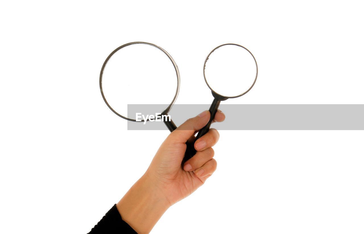 Cropped hand of woman holding magnifying glasses against white background