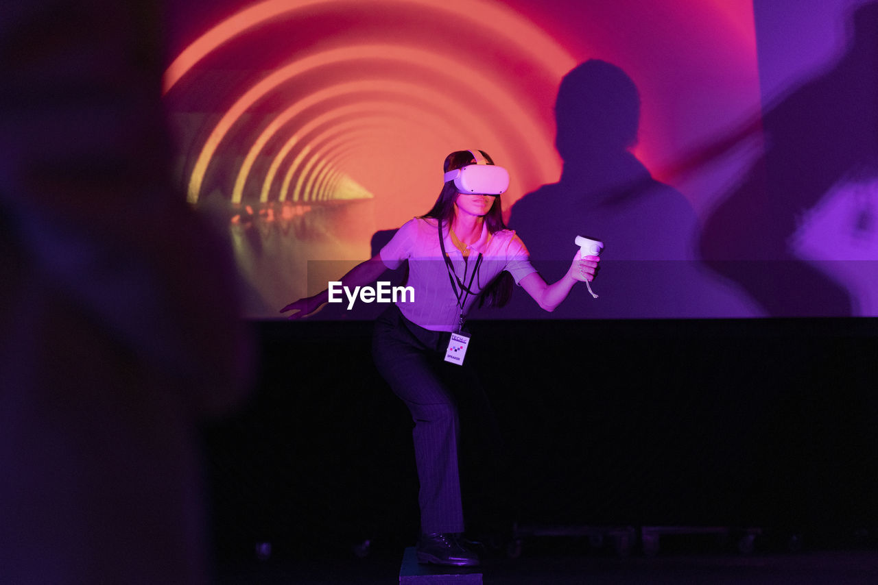 Businesswoman with joystick wearing futuristic glasses standing against projection screen in workshop