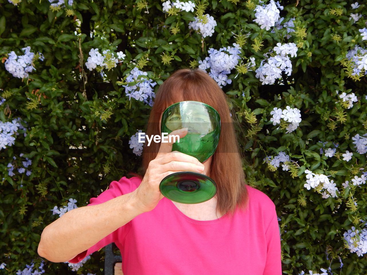 Portrait of woman holding large green glass against flowering plants