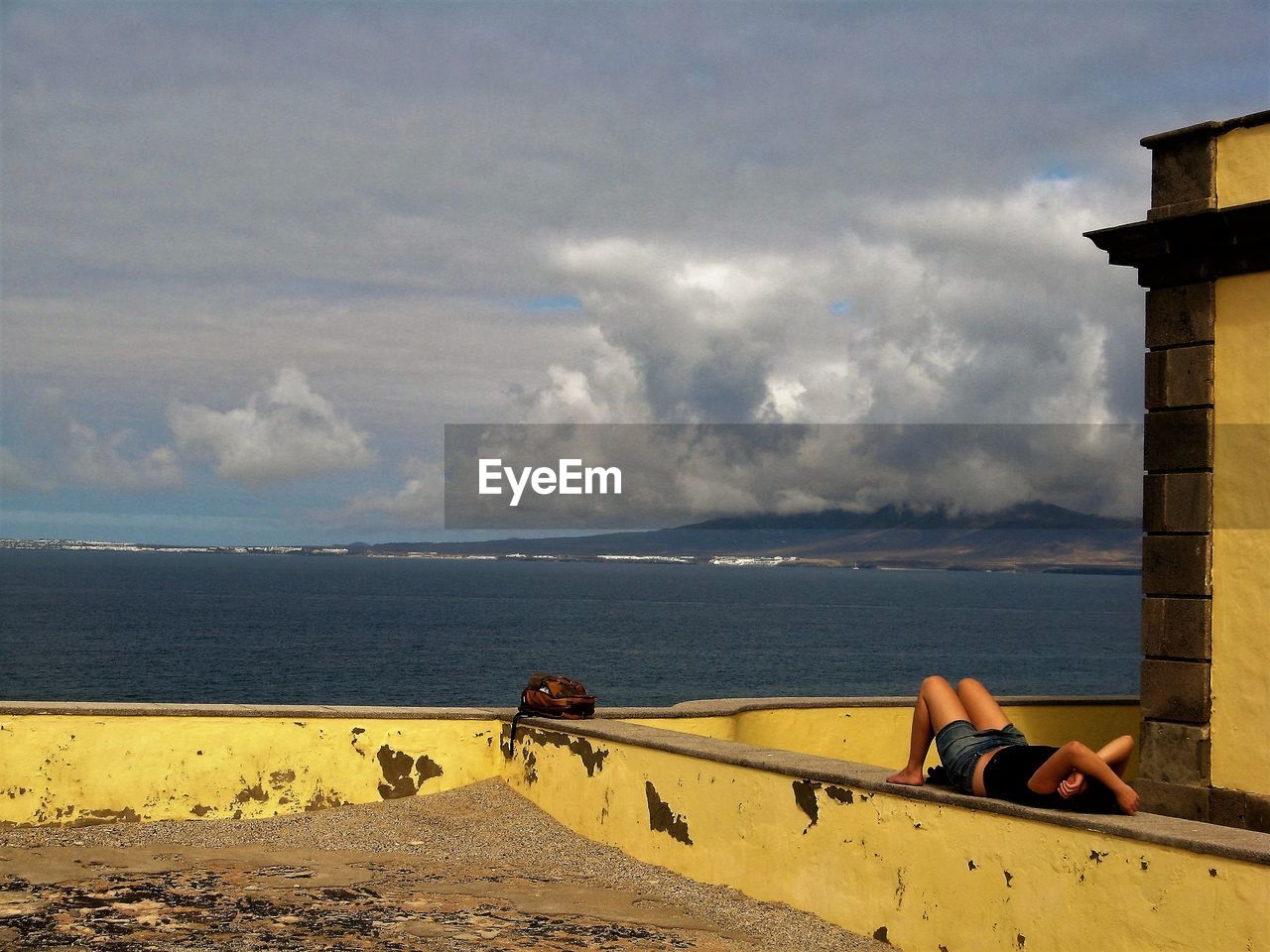 Woman resting on retaining wall by sea against sky