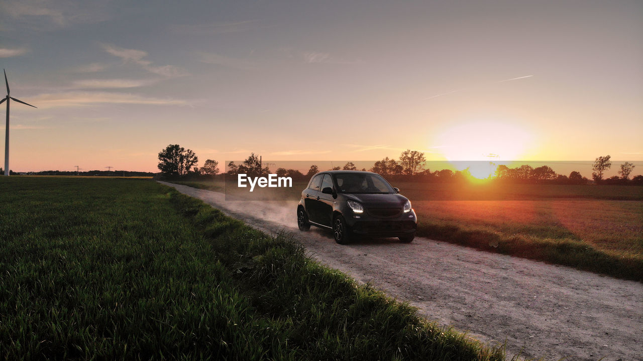 CARS ON ROAD AMIDST FIELD DURING SUNSET