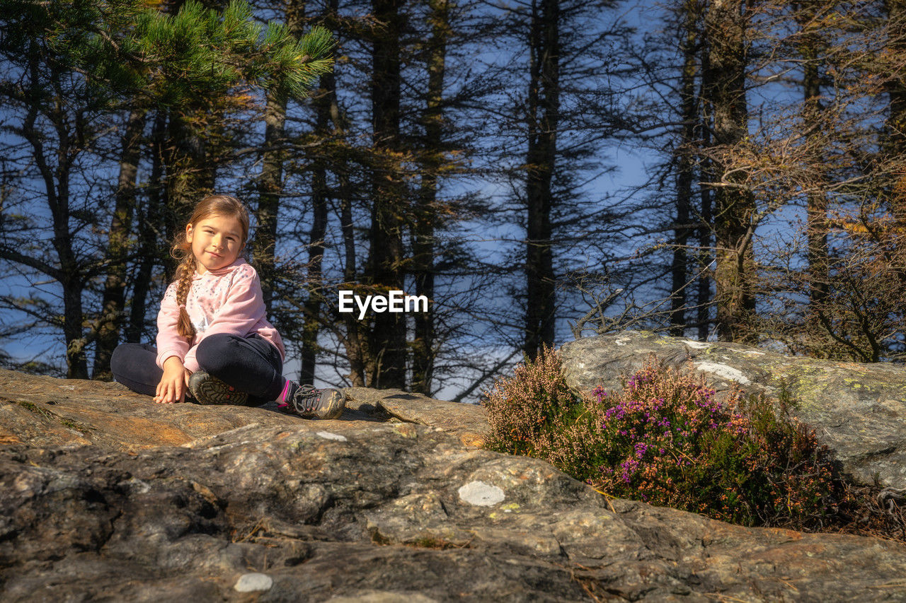 Girl sitting on a rock in a forest, illuminated by sunlight. glendalough, wicklow mountains, ireland