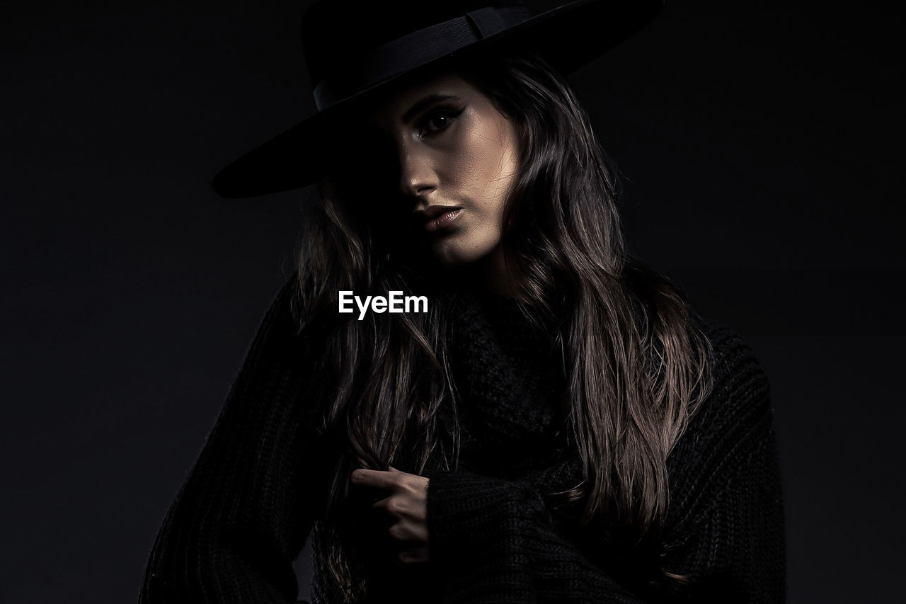 black, one person, portrait, hat, adult, clothing, darkness, studio shot, young adult, long hair, women, dark, indoors, black background, fedora, looking at camera, black and white, fashion, hairstyle, looking, fashion accessory, serious, person, front view, monochrome, monochrome photography, headshot, emotion, photo shoot