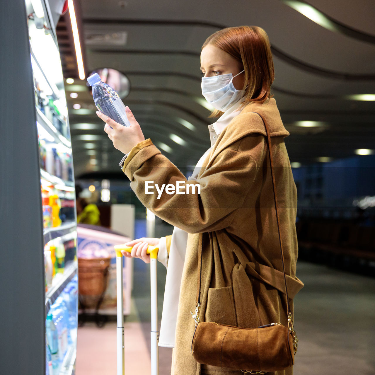 Side view of woman wearing mask buying water bottle at airport