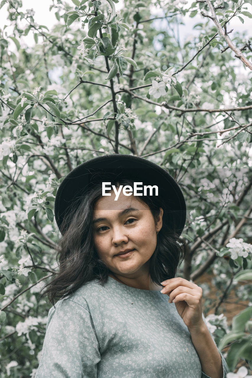 Beautiful asian plus size model wearing green dress enjoying smell of blooming spring tree outdoor