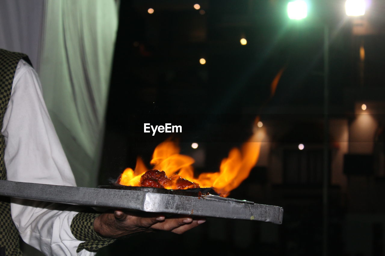 Midsection of waiter holding burning food in tray restaurant
