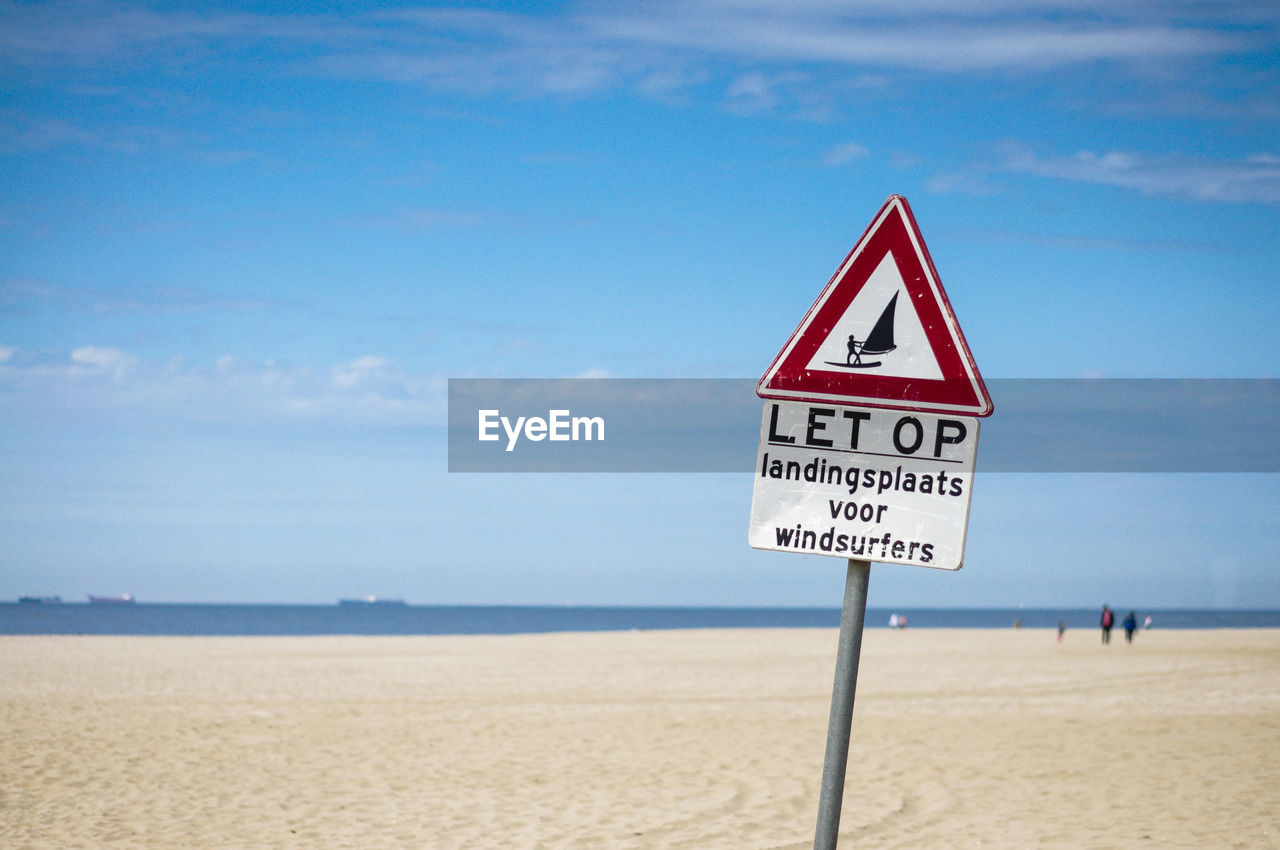 Curious information sign on beach against sky