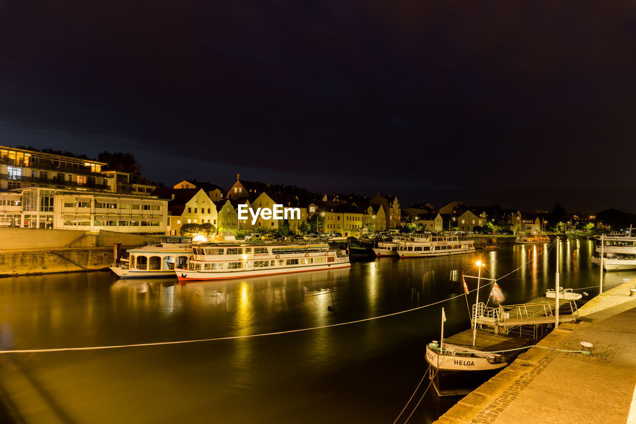 ILLUMINATED BUILDINGS BY RIVER AGAINST SKY