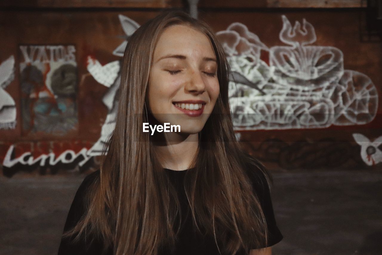 Smiling young woman with eyes closed against wall