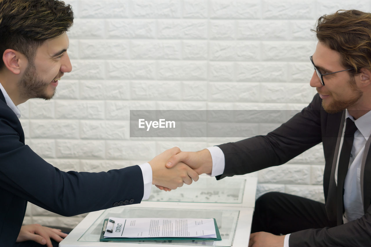 Businessmen shaking hands while sitting at table in office