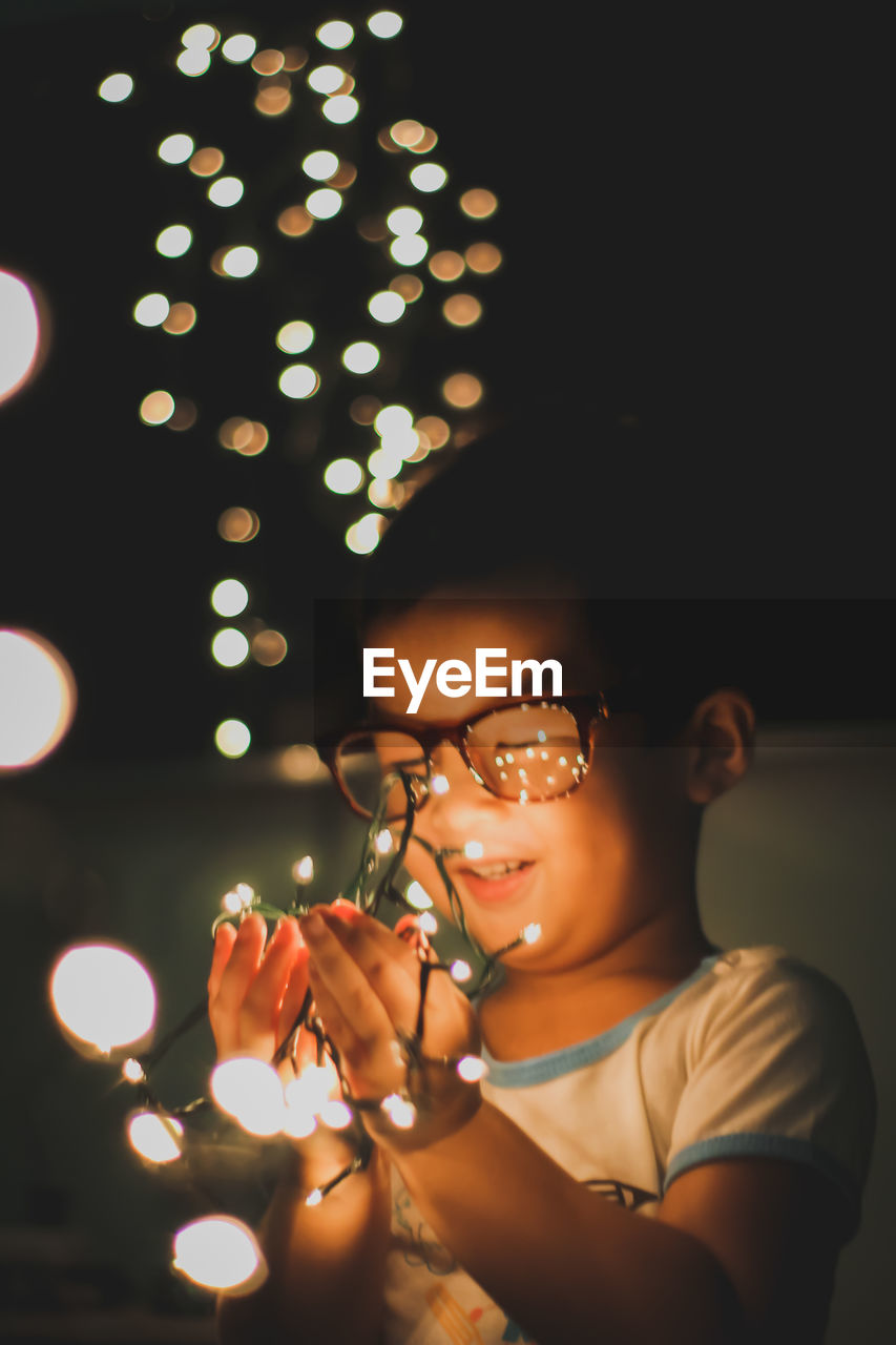 CLOSE-UP OF YOUNG WOMAN HOLDING ILLUMINATED CHRISTMAS LIGHTS AT HOME